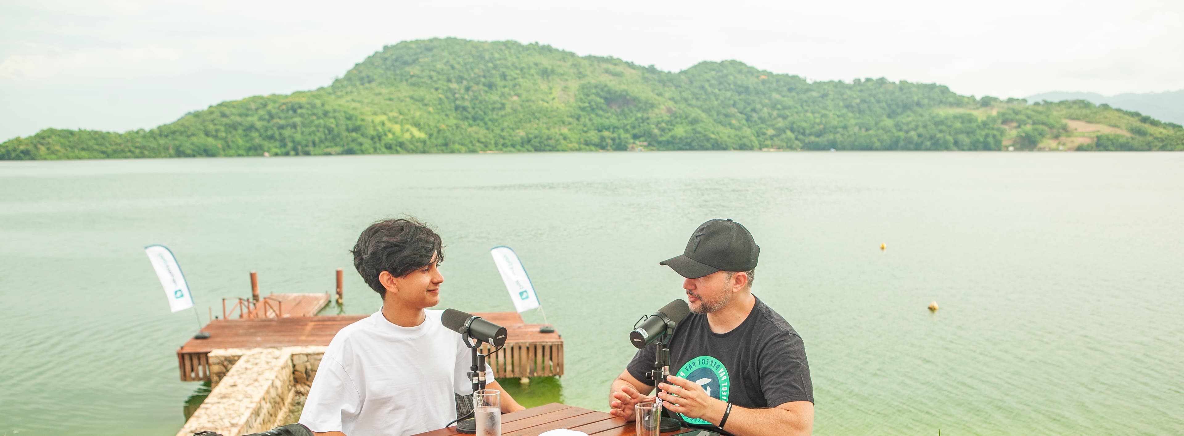 Arthur Oliveira gravando podcast ao ar livre em frente ao lago com montanha ao fundo